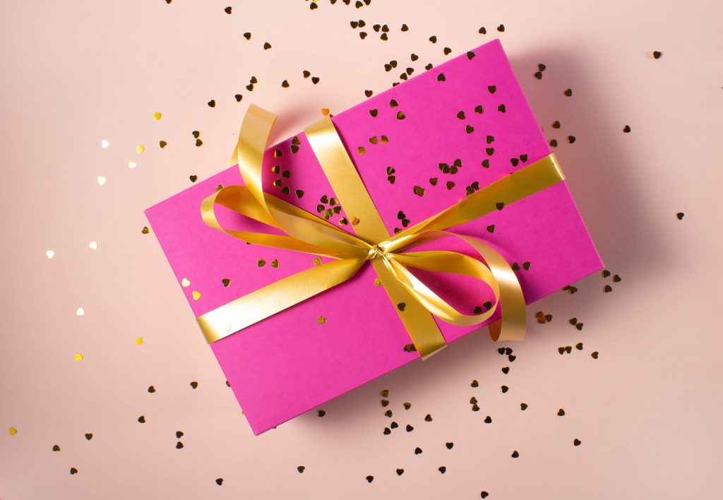 A dark pink gift with a gold bow on a light pink background